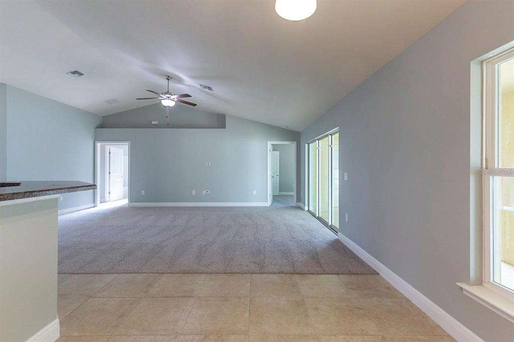 A living room with vaulted ceilings, gray walls, carpeted flooring, and sliding glass doors — 3401 EVERETT TERRACE, NORTH PORT, FL