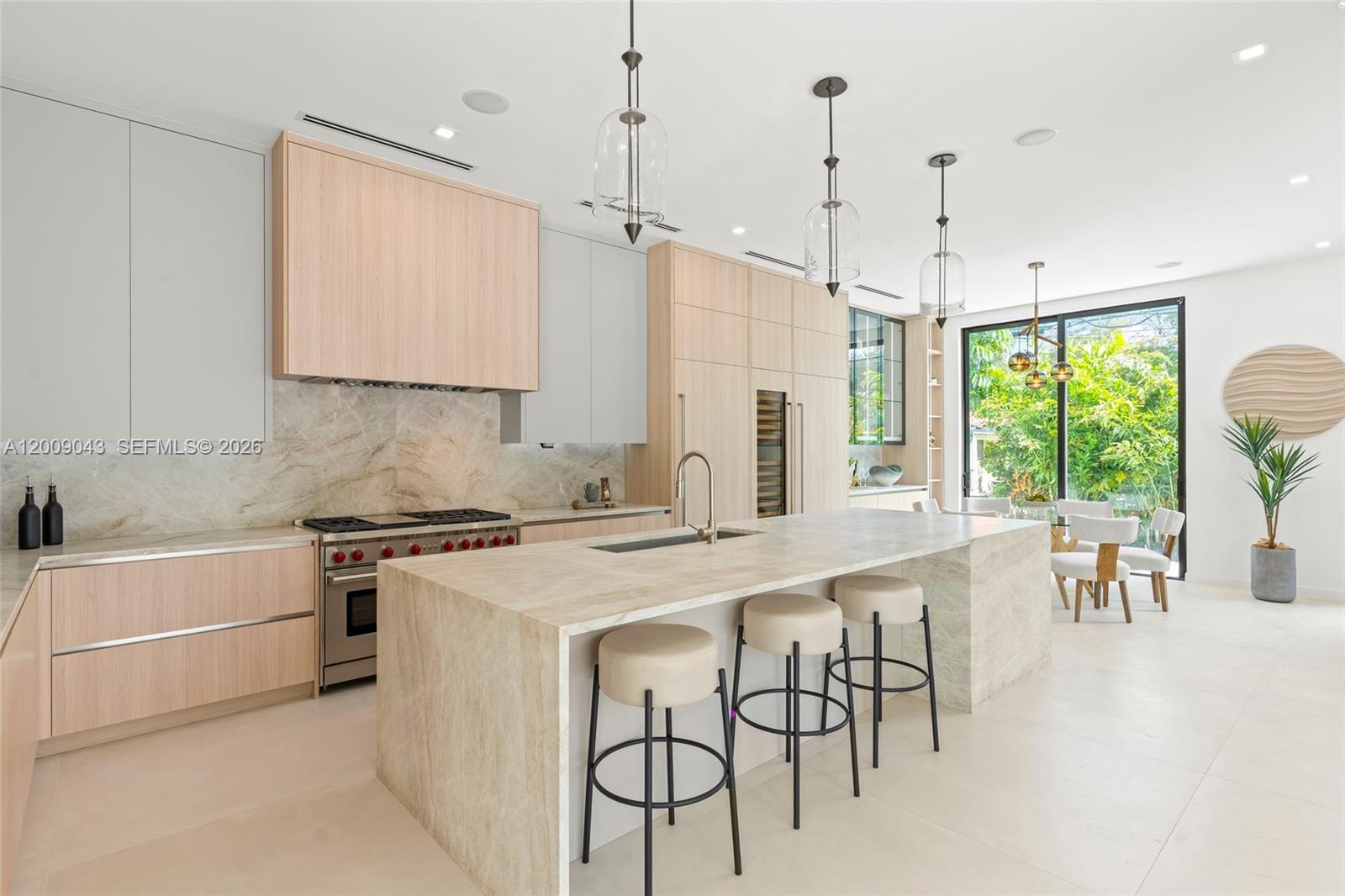 A modern kitchen features light wood cabinetry, a stone island with bar stools, and dining area — 730 Zamora Ave, Coral Gables FL 33134, CORAL GABLES, FL