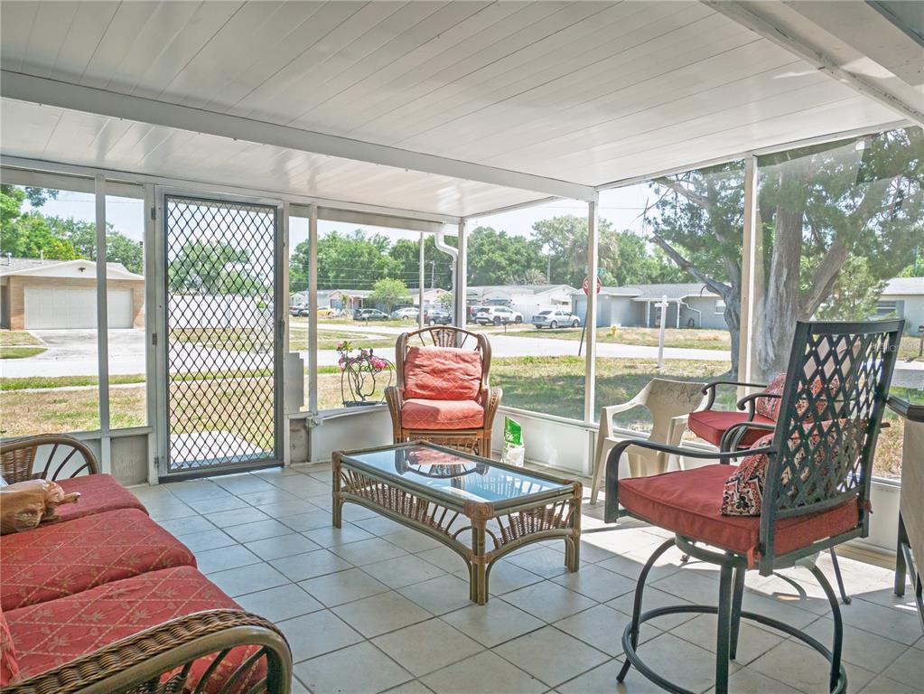 A screened-in porch features tiled flooring, wicker furniture with red cushions, and a glass-topped table — 6436 CARDINAL DR, CLEARWATER, FL