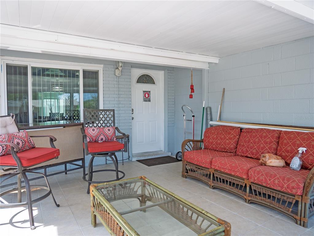 A covered patio features light-colored tile flooring, a wicker sofa, chairs, and a glass-topped table — 6436 CARDINAL DR, CLEARWATER, FL