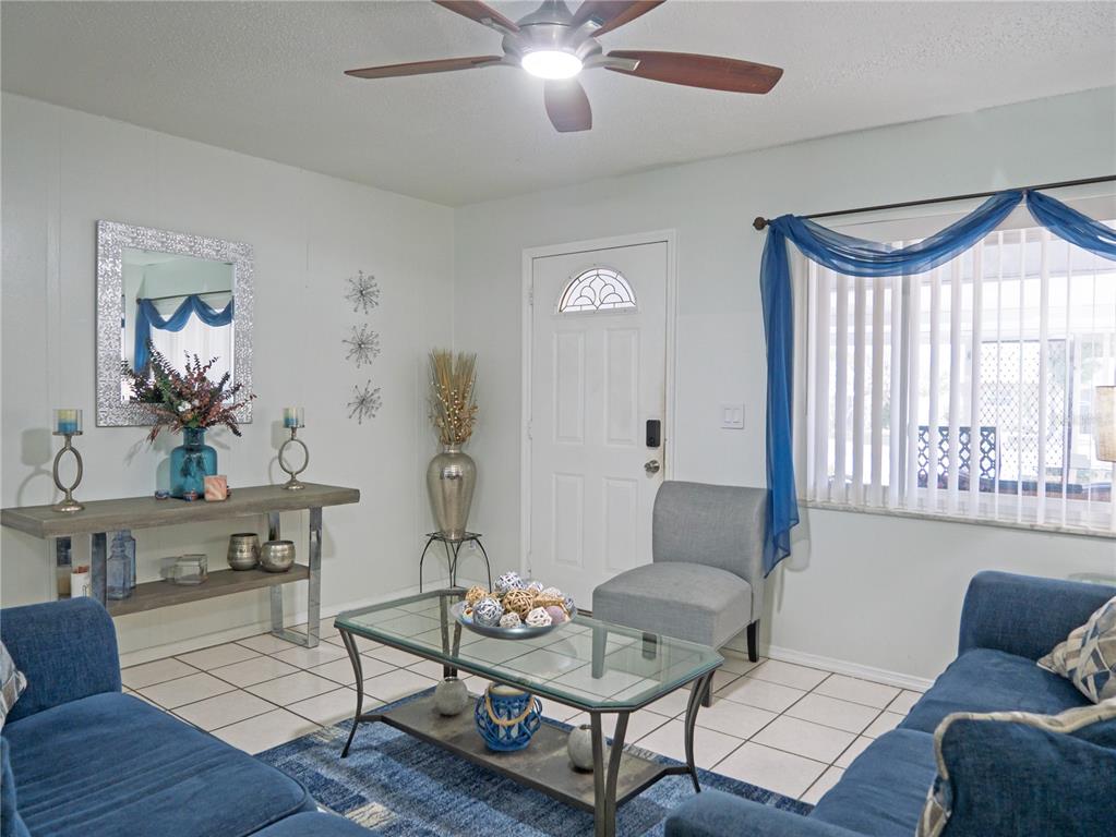 A living room features blue sofas, a glass coffee table, and tile flooring — 6436 CARDINAL DR, CLEARWATER, FL