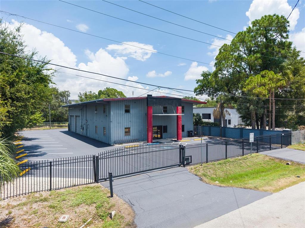 An exterior view of a gray industrial building with red pillars and a fenced parking lot — 5021 W NASSAU STREET, TAMPA, FL