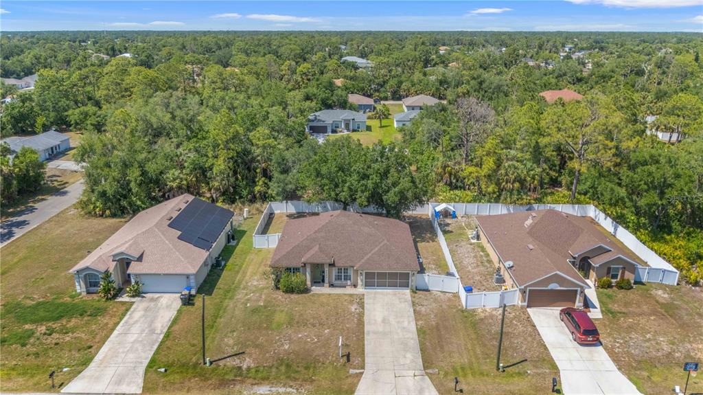 An aerial view shows three suburban houses with driveways and fenced backyards surrounded by trees — 3680 CHANNING AVENUE, NORTH PORT, FL