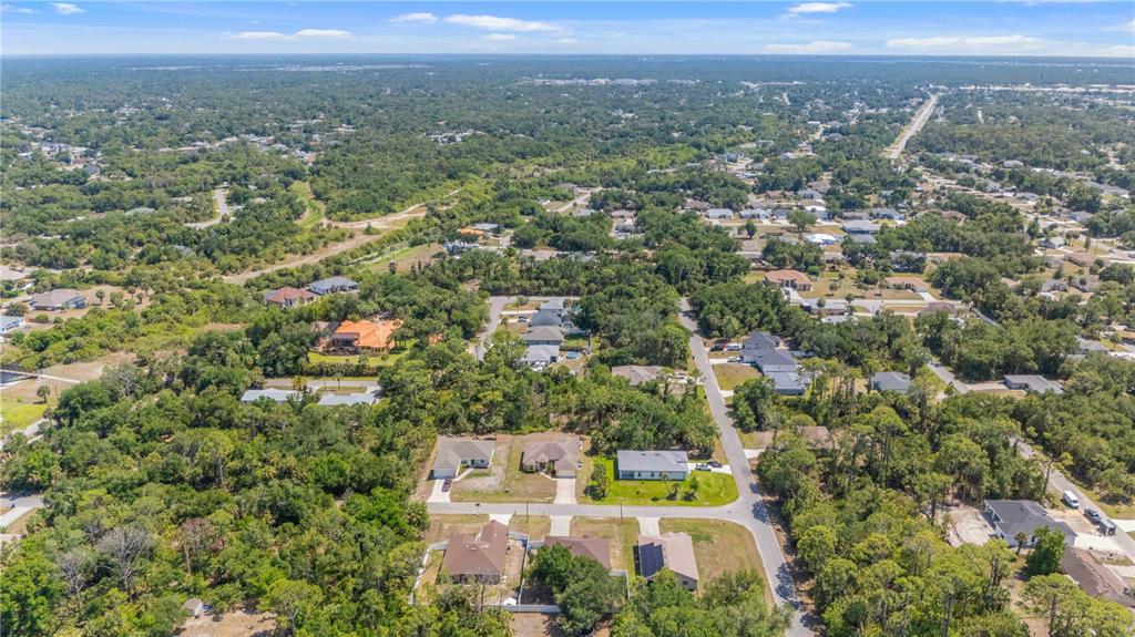 An aerial view shows a suburban neighborhood with houses surrounded by dense green trees — 3680 CHANNING AVENUE, NORTH PORT, FL