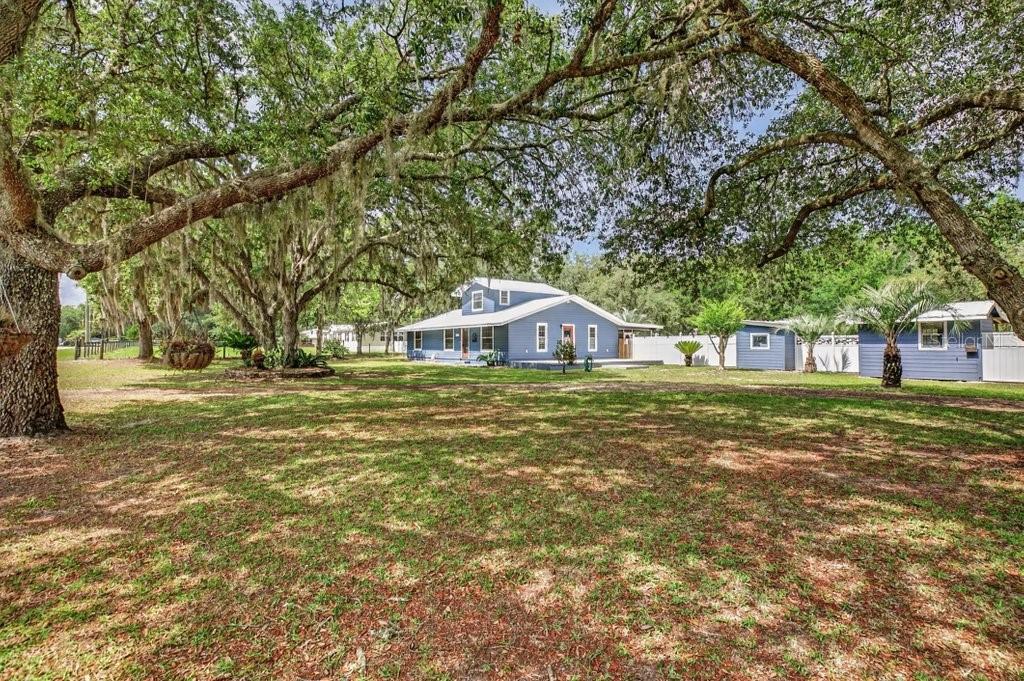 A blue two-story house sits on a grassy lot shaded by large oak trees — 121 DAREN DRIVE, PALATKA, FL