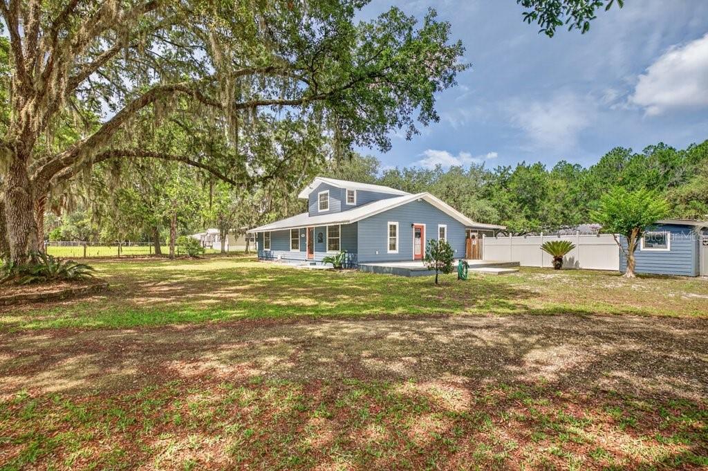 A blue two-story house with a white fence and large trees in the yard — 121 DAREN DRIVE, PALATKA, FL
