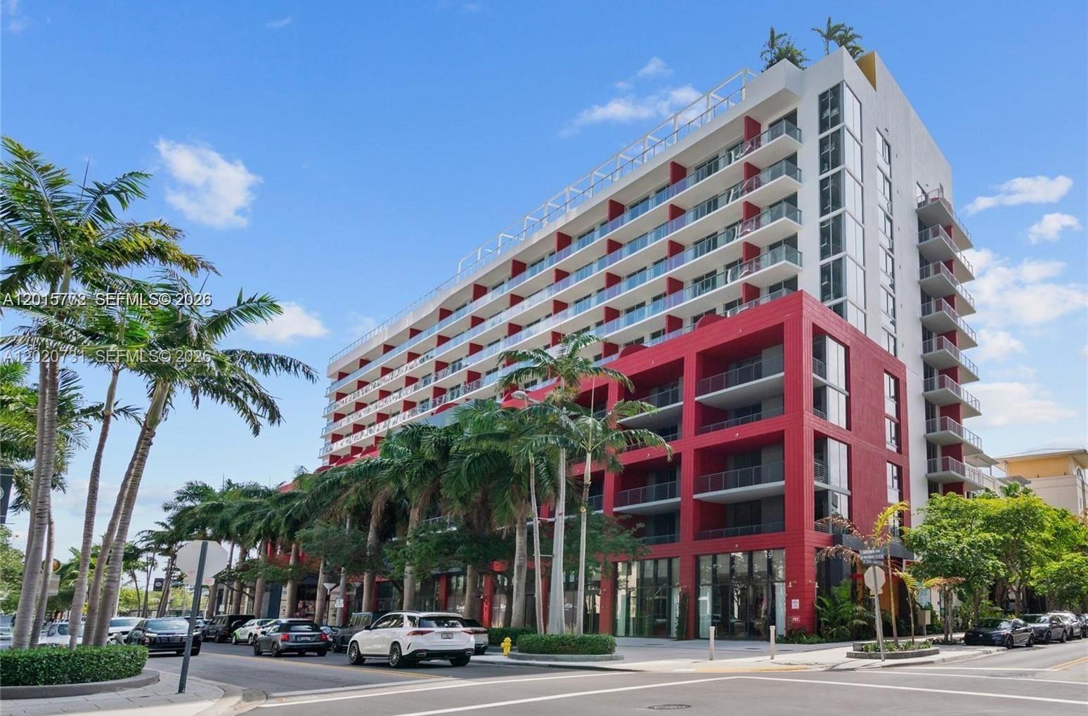 A multi-story building with red accents and balconies stands above a street with cars — 90 NE 32 # 905, Miami FL 33137, MIAMI, FL