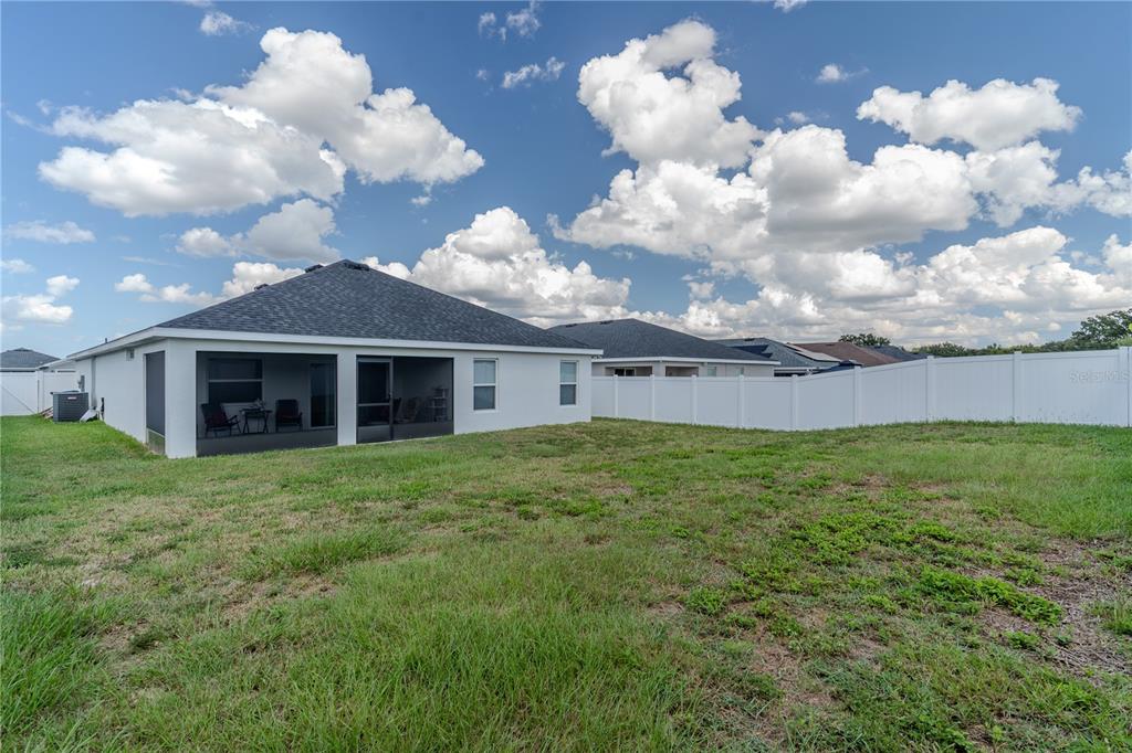 The backyard of a single-story house features a screened-in patio and a white vinyl fence — 629 FAIRHOPE DRIVE, POLK CITY, FL