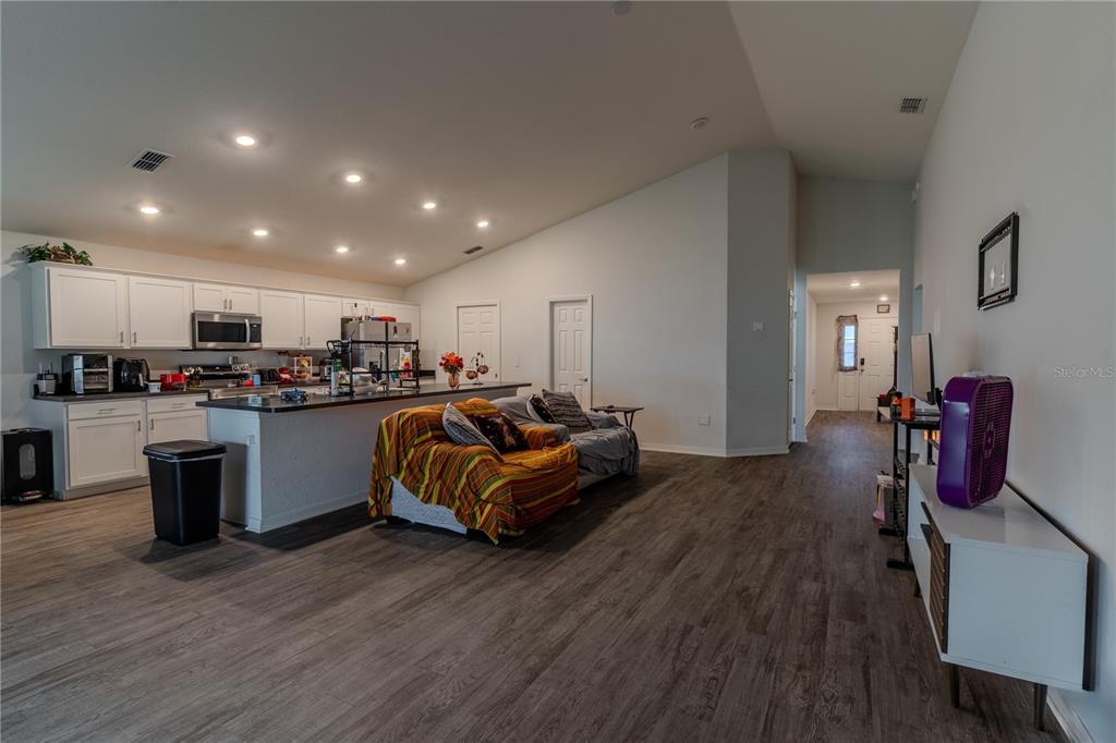 An open-concept kitchen and living area features white cabinetry, a kitchen island, and wood-look flooring — 629 FAIRHOPE DRIVE, POLK CITY, FL