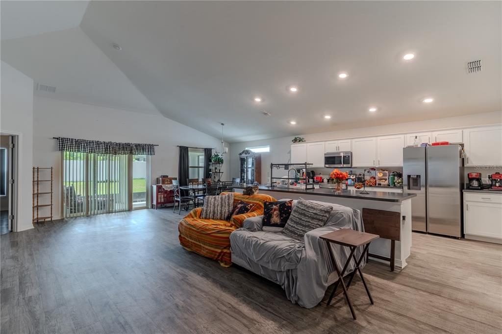 An open-concept kitchen and living area features white cabinets, stainless appliances, and wood-look flooring — 629 FAIRHOPE DRIVE, POLK CITY, FL