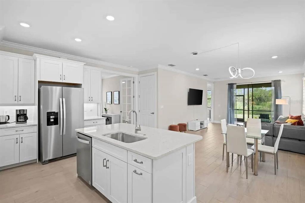 A modern kitchen with white cabinetry and a central island opens into a living area — 245 TERAMO WAY, NOKOMIS, FL