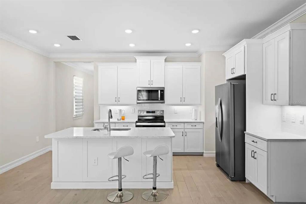 A modern white kitchen features a central island with bar stools and stainless steel appliances — 245 TERAMO WAY, NOKOMIS, FL