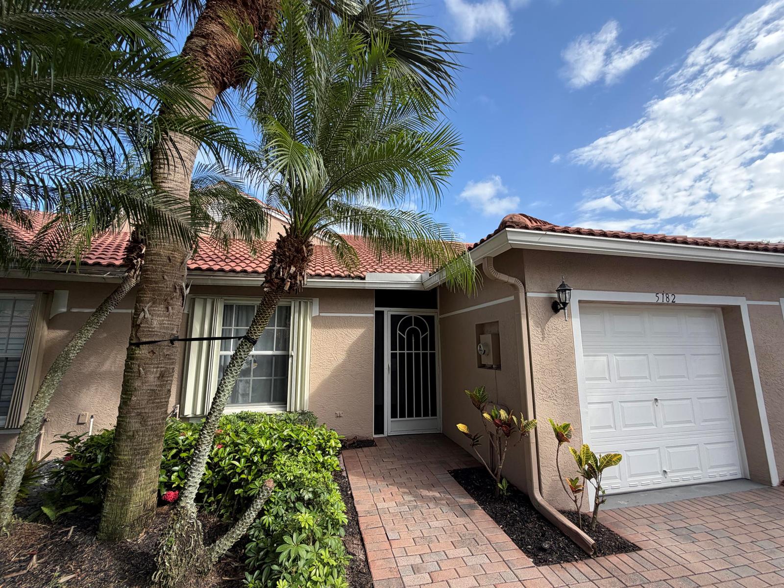 A beige house exterior features a palm tree, a brick walkway, and a white garage — 5182 Toscana Trail, Boynton Beach FL 33437, BOYNTON BEACH, FL