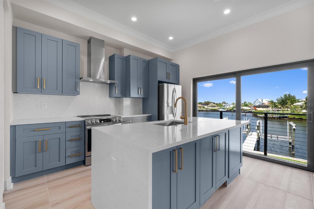 A modern kitchen features blue cabinets, white quartz countertops, and a view of a canal — 772 GRAN KAYMEN WAY, APOLLO BEACH, FL