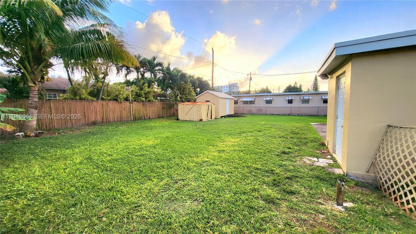 A grassy backyard features a wooden fence, a small shed, and a palm tree — 720 NE 5th St # 1, Hallandale Beach FL 33009, HALLANDALE BEACH, FL