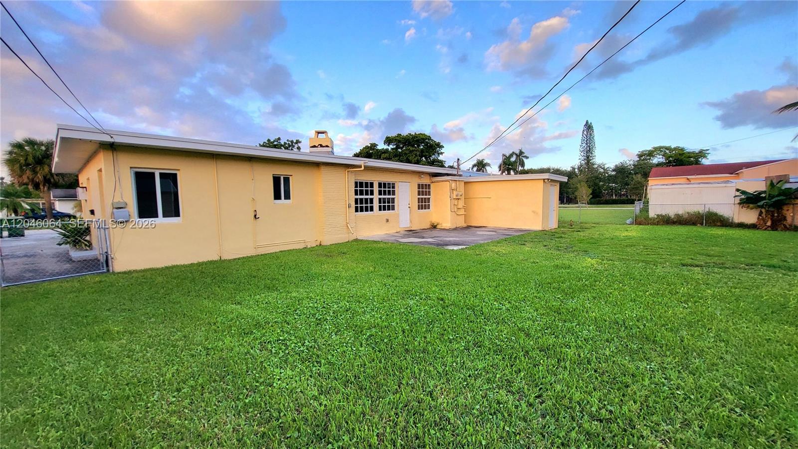 The exterior of a yellow, single-story house features a large grassy backyard — 720 NE 5th St # 1, Hallandale Beach FL 33009, HALLANDALE BEACH, FL