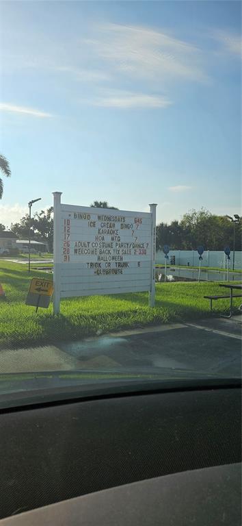 A community sign displays a schedule of events on a grassy lot near a pond — 8410 WAGON WHEEL CIRCLE, NORTH FORT MYERS, FL