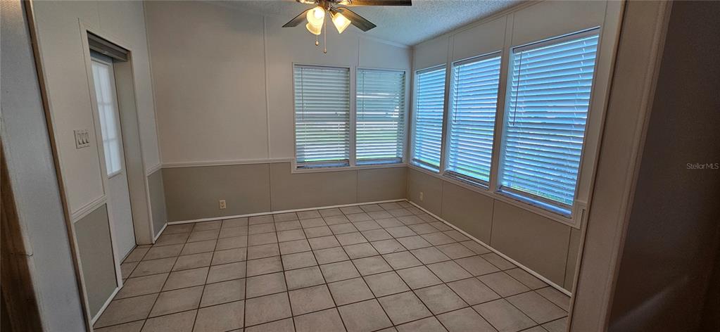 A sunroom with tiled flooring, white paneled walls, and multiple windows with horizontal blinds — 8410 WAGON WHEEL CIRCLE, NORTH FORT MYERS, FL