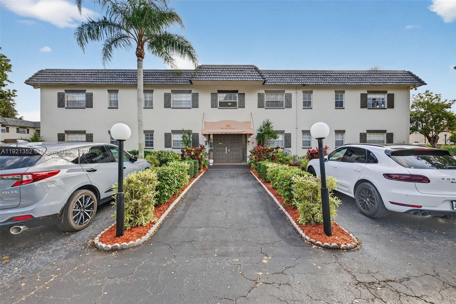 The exterior of a two-story apartment building features a central entrance with a tan awning — 5681 SW 2nd Ct # 117, Margate FL 33068, MARGATE, FL