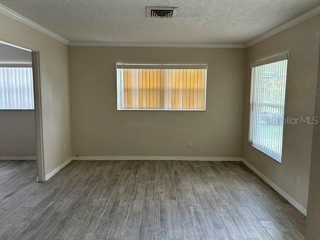 An empty room features light-colored wood-look tile flooring, beige walls, and two windows with blinds — 1404 SANDALWOOD DRIVE, DUNEDIN, FL