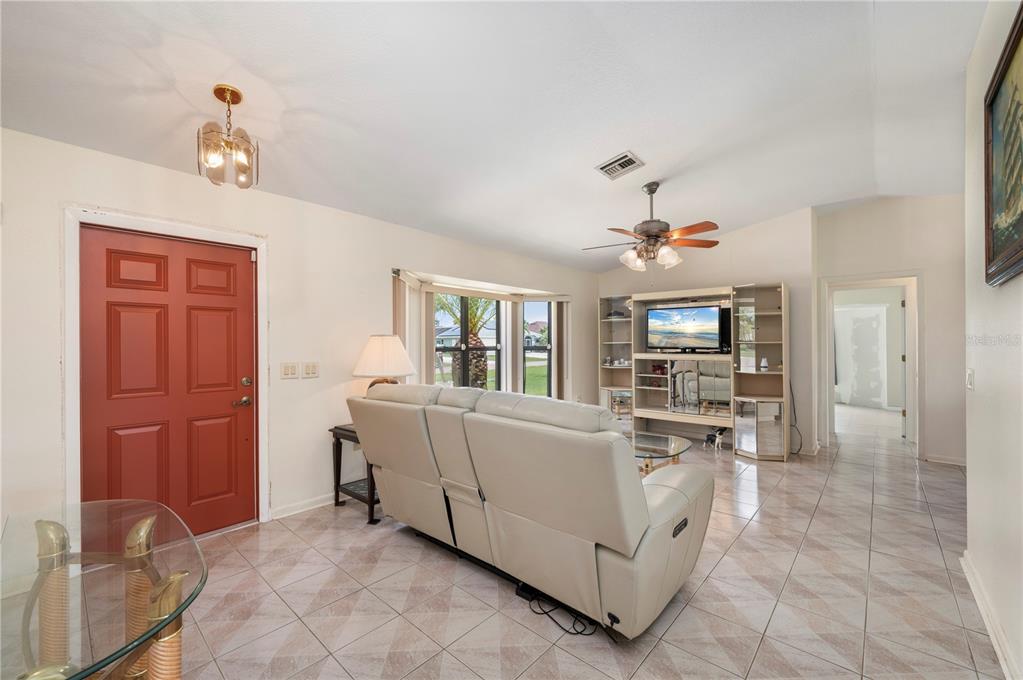A living room with tile floors, a beige sofa, a television unit, and a red door — 1659 BLUE LAKE CIRCLE, PUNTA GORDA, FL