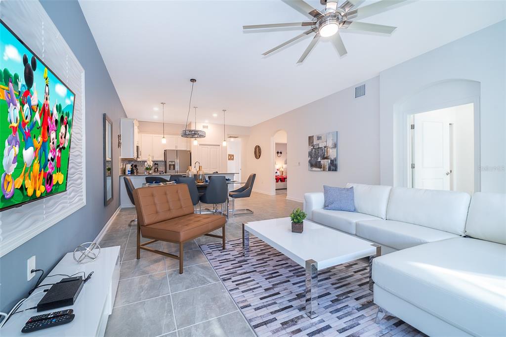 A modern open-concept living and dining area features tile flooring, white furniture, and a television — 8889 CABOT CLIFFS DRIVE UNIT 101, DAVENPORT, FL