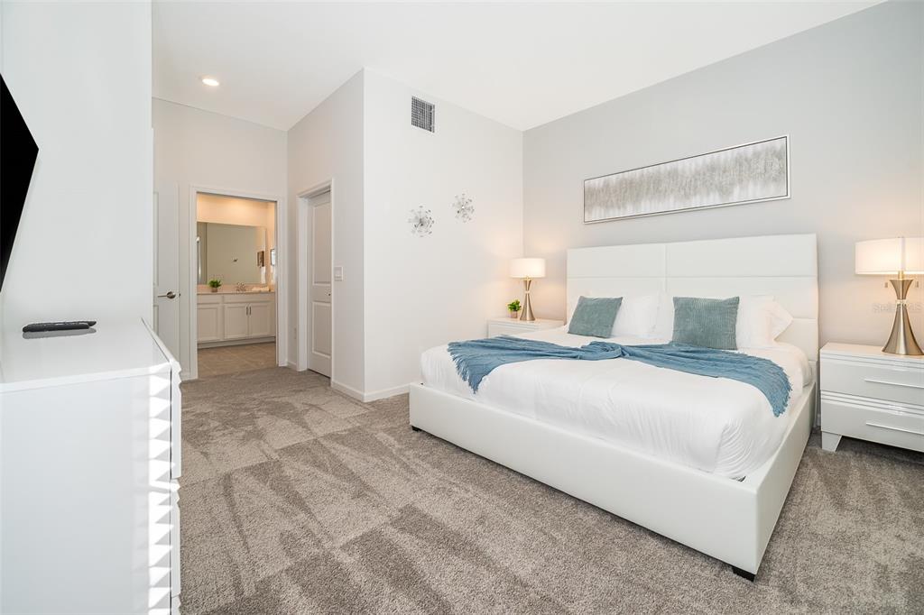 A bedroom features a white bed, gray carpet, and an attached bathroom doorway — 8889 CABOT CLIFFS DRIVE UNIT 101, DAVENPORT, FL