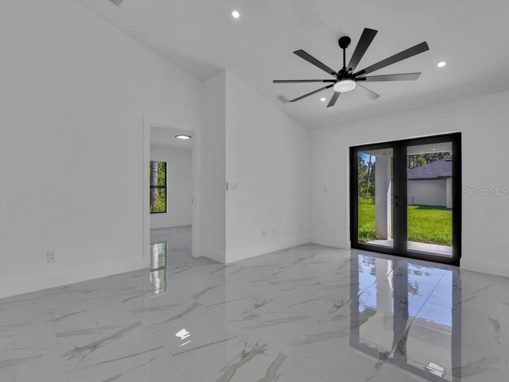 A bright room with white walls, marble-look tile floors, a ceiling fan, and glass doors — 4747 13TH STREET SW, LEHIGH ACRES, FL