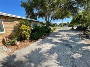 A gravel driveway leads past the side of a house with wood-paneled siding and landscaping — 6901 GULF WINDS DRIVE, ST PETE BEACH, FL