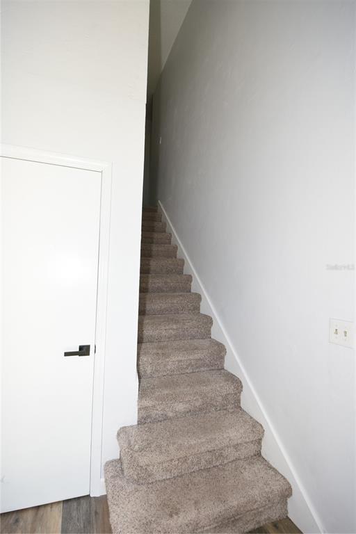 A carpeted staircase ascends along a white wall next to a closed white door — 4 SOUTHBURY COURT UNIT 4, PALM COAST, FL