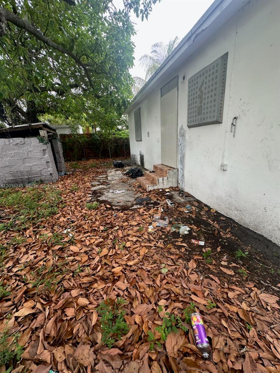 An exterior view of a white building with a metal security screen and debris-covered ground — 1891 NW 62nd Ter, Miami FL 33147, MIAMI, FL
