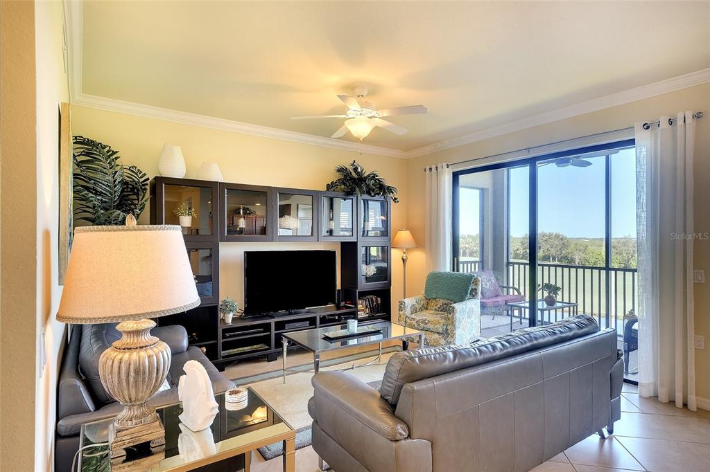 A living room features a dark entertainment center, leather sofas, and a sliding door to a balcony — 7121 RIVER HAMMOCK DRIVE UNIT 303, BRADENTON, FL