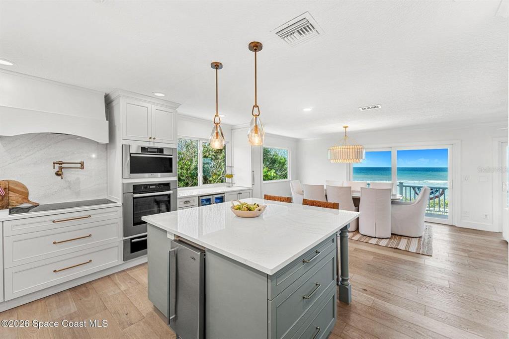 A modern kitchen features a gray island, white cabinetry, and a dining area overlooking the ocean — 6105 S HIGHWAY A1A, MELBOURNE BEACH, FL