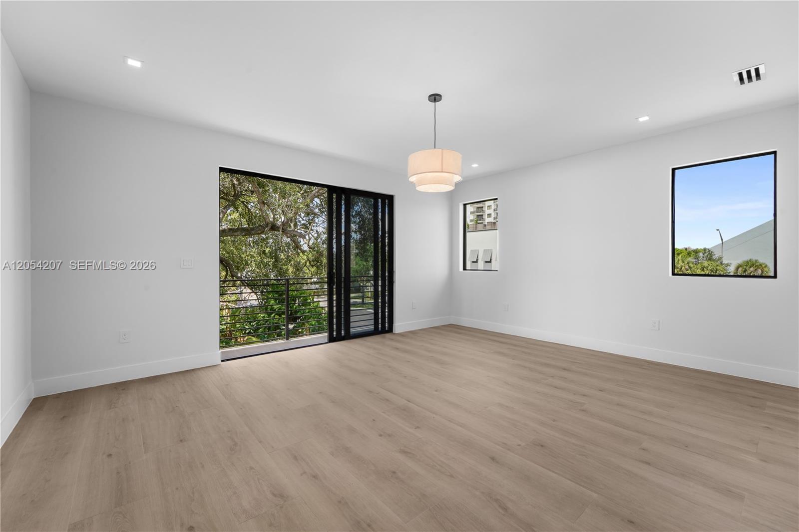 A bright, empty room features light wood flooring, white walls, a modern pendant light, and sliding glass doors — 2735 SW 23rd Ter, Miami FL 33145, MIAMI, FL