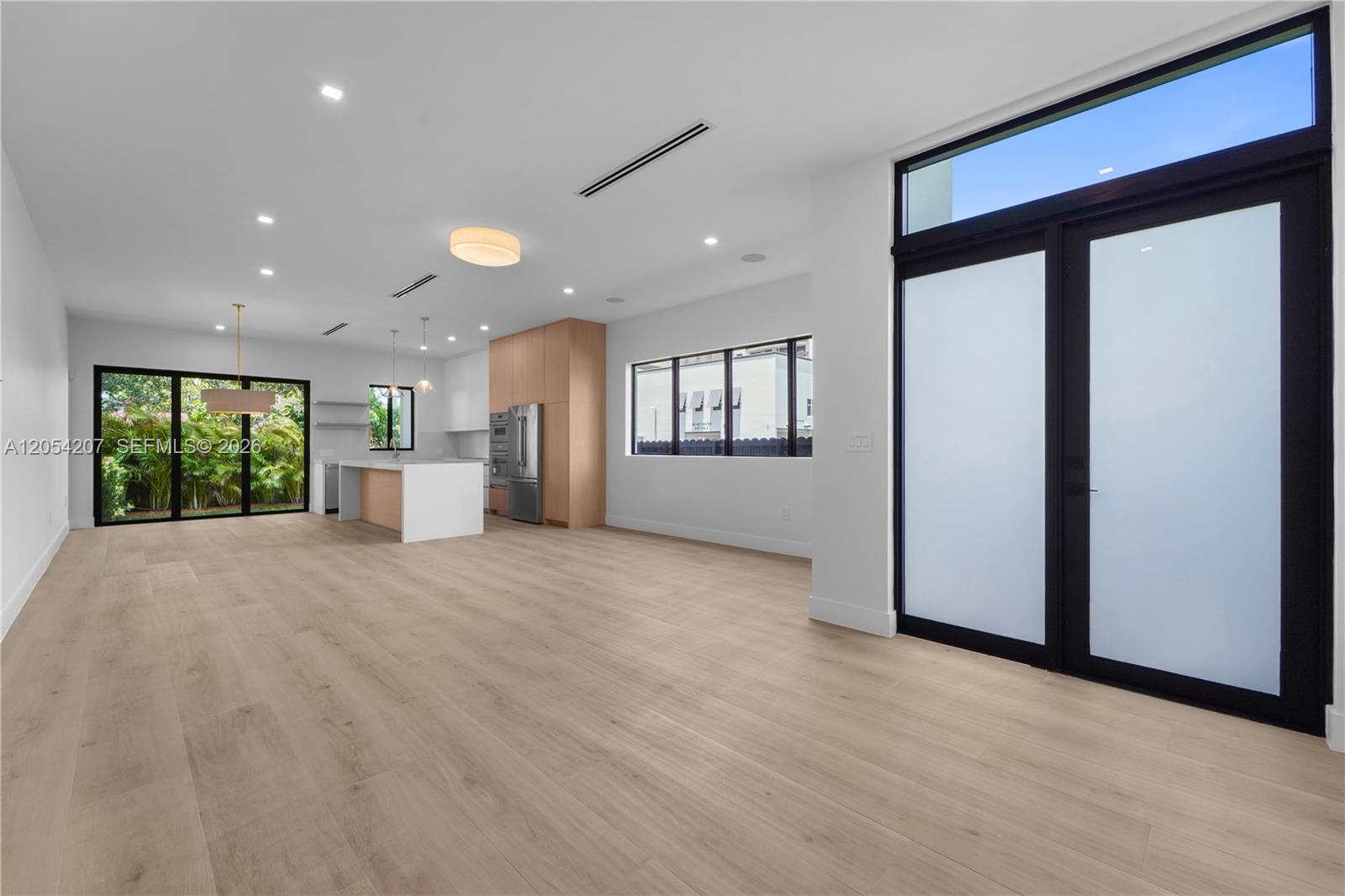 A modern open-concept kitchen and living area features light wood flooring and large glass doors — 2735 SW 23rd Ter, Miami FL 33145, MIAMI, FL