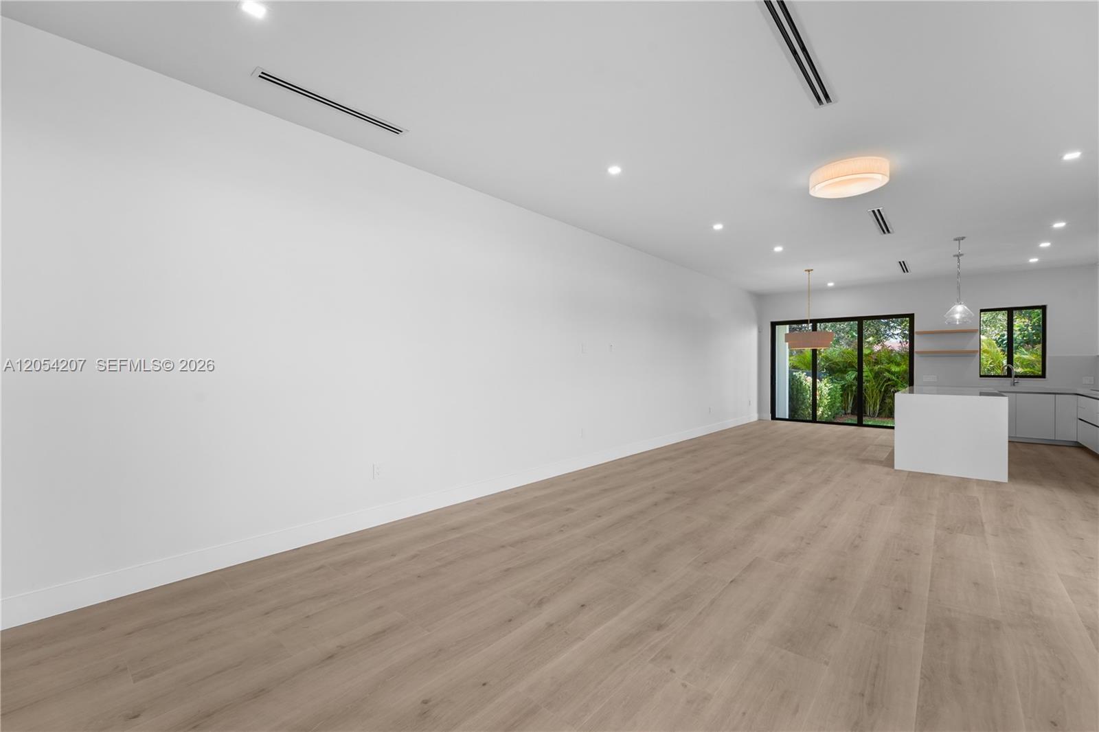 This open-concept room features light wood-look flooring, white walls, and a modern kitchen area — 2735 SW 23rd Ter, Miami FL 33145, MIAMI, FL