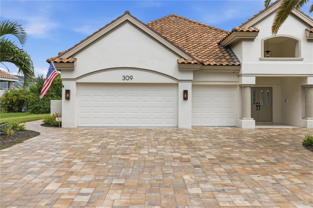 A house exterior features a paved driveway, a three-car garage, and a tiled roof — 309 S STONE BRIAR CREEK DRIVE, VENICE, FL