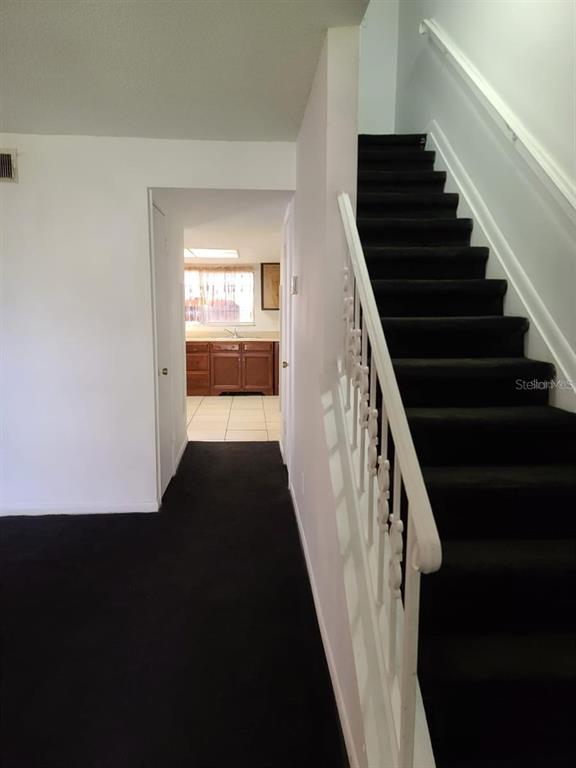 An interior view shows a carpeted staircase with a white railing leading to a kitchen — 2222 SILVER PINES PLACE UNIT 902, ORLANDO, FL