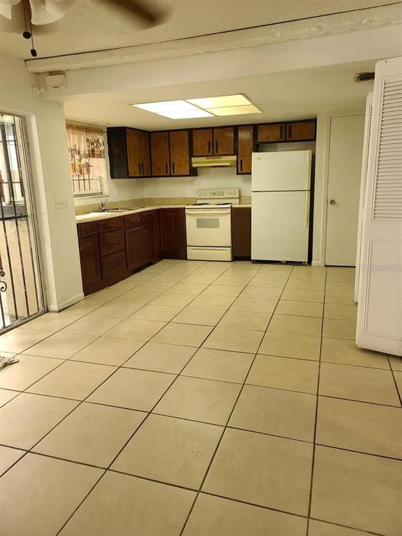 A kitchen features dark wood cabinets, white appliances, and light-colored tile flooring — 2222 SILVER PINES PLACE UNIT 902, ORLANDO, FL
