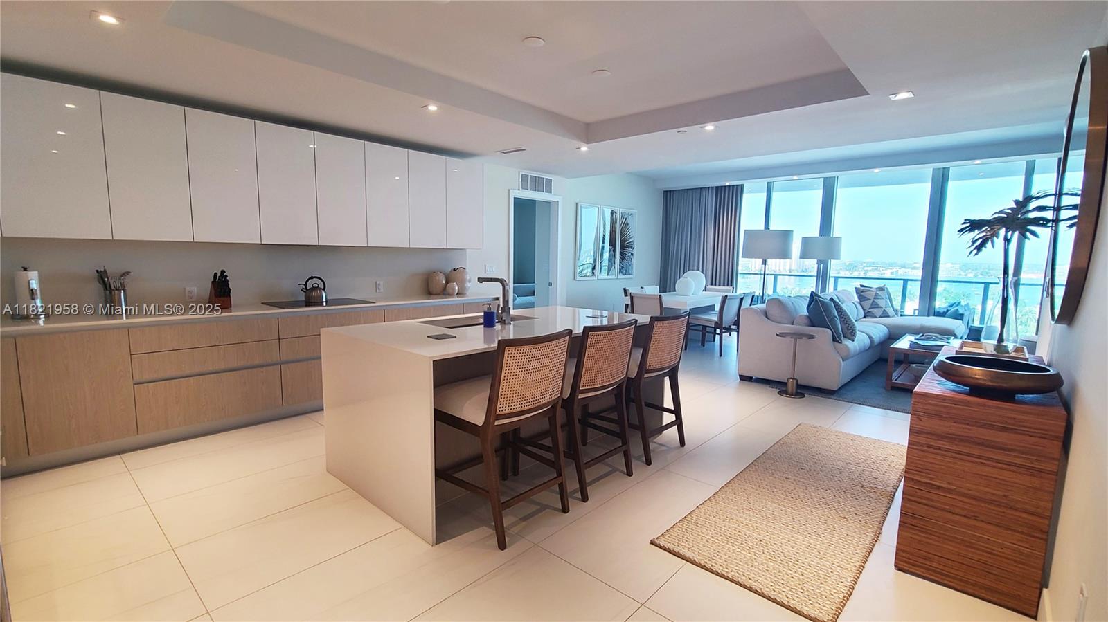 A modern open-concept kitchen and living area features white cabinetry, a central island, and floor-to-ceiling windows — 3100 N Ocean Drive # 1206, Singer Island FL 33404, SINGER ISLAND, FL