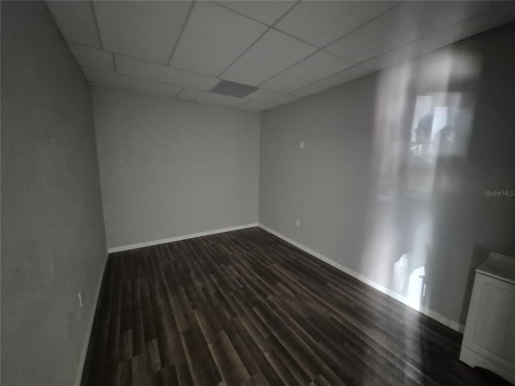An empty room features gray walls, a drop ceiling, and dark wood-look flooring — 5434 LAND O LAKES BOULEVARD, LAND O LAKES, FL