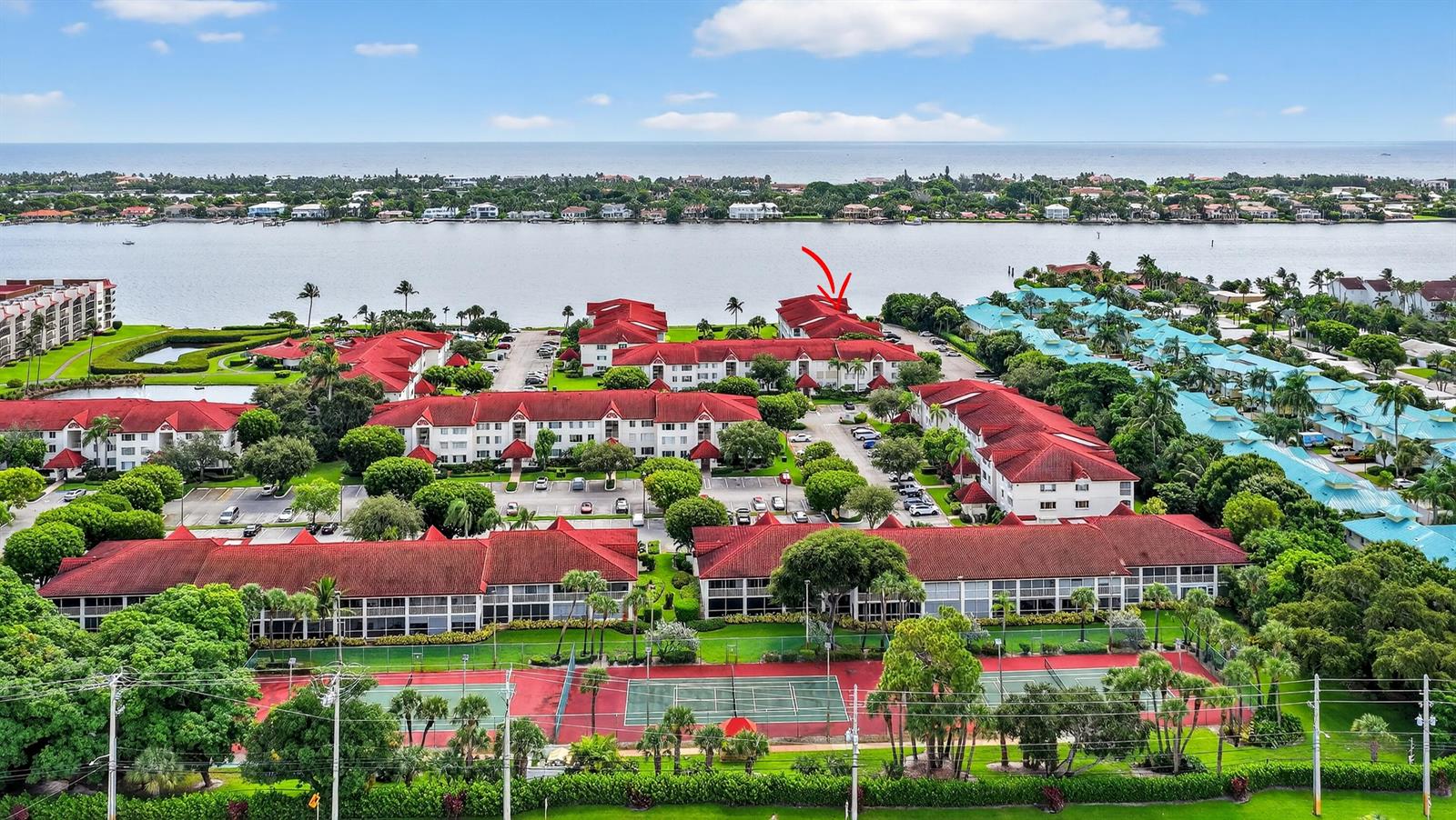 An aerial view of a residential complex with red-roofed buildings and tennis courts near water — 110 Half Moon Circle # D2, Hypoluxo FL 33462, HYPOLUXO, FL