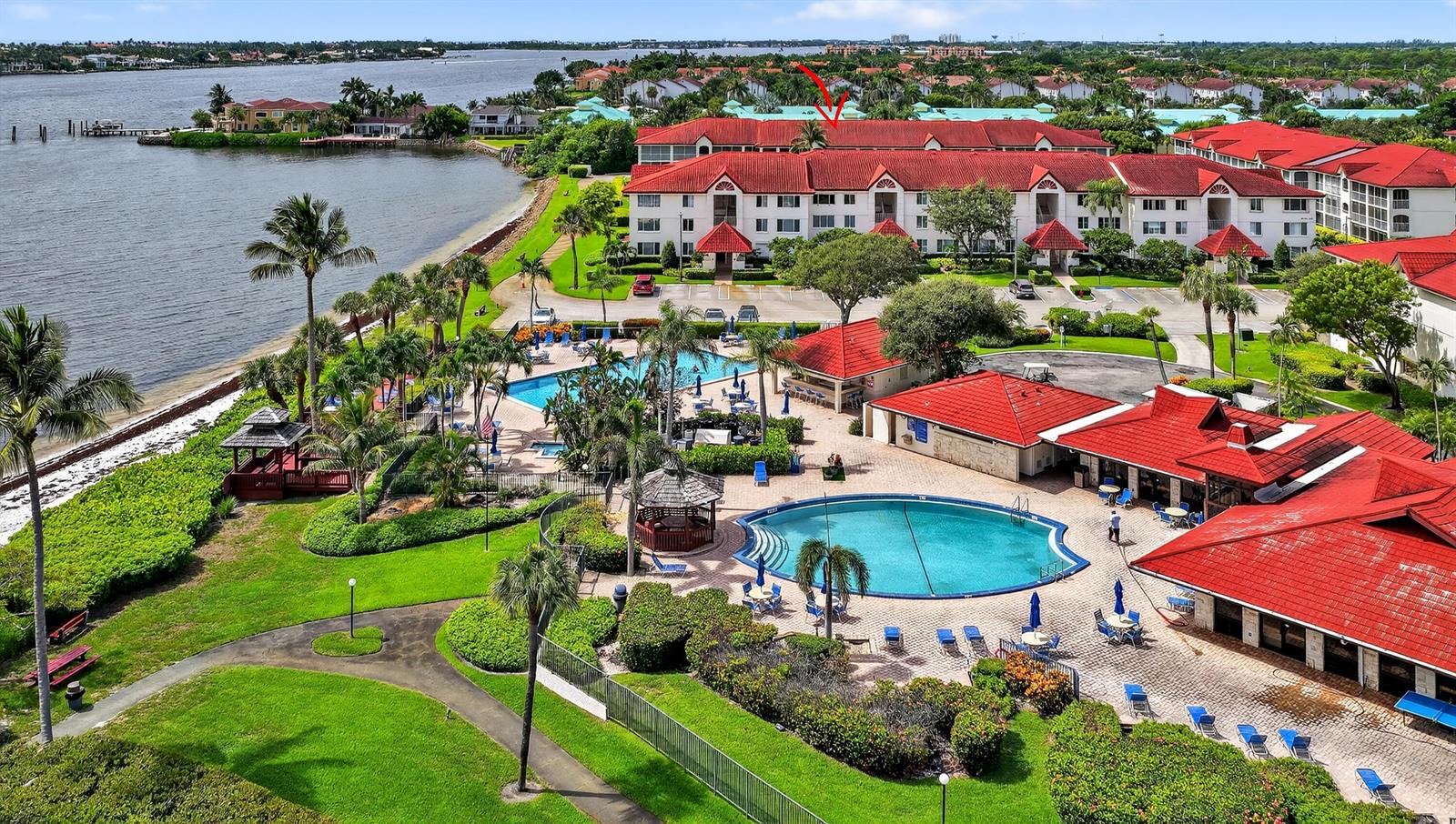 An aerial view shows a waterfront condominium complex with red roofs, swimming pools, and landscaping — 110 Half Moon Circle # D2, Hypoluxo FL 33462, HYPOLUXO, FL
