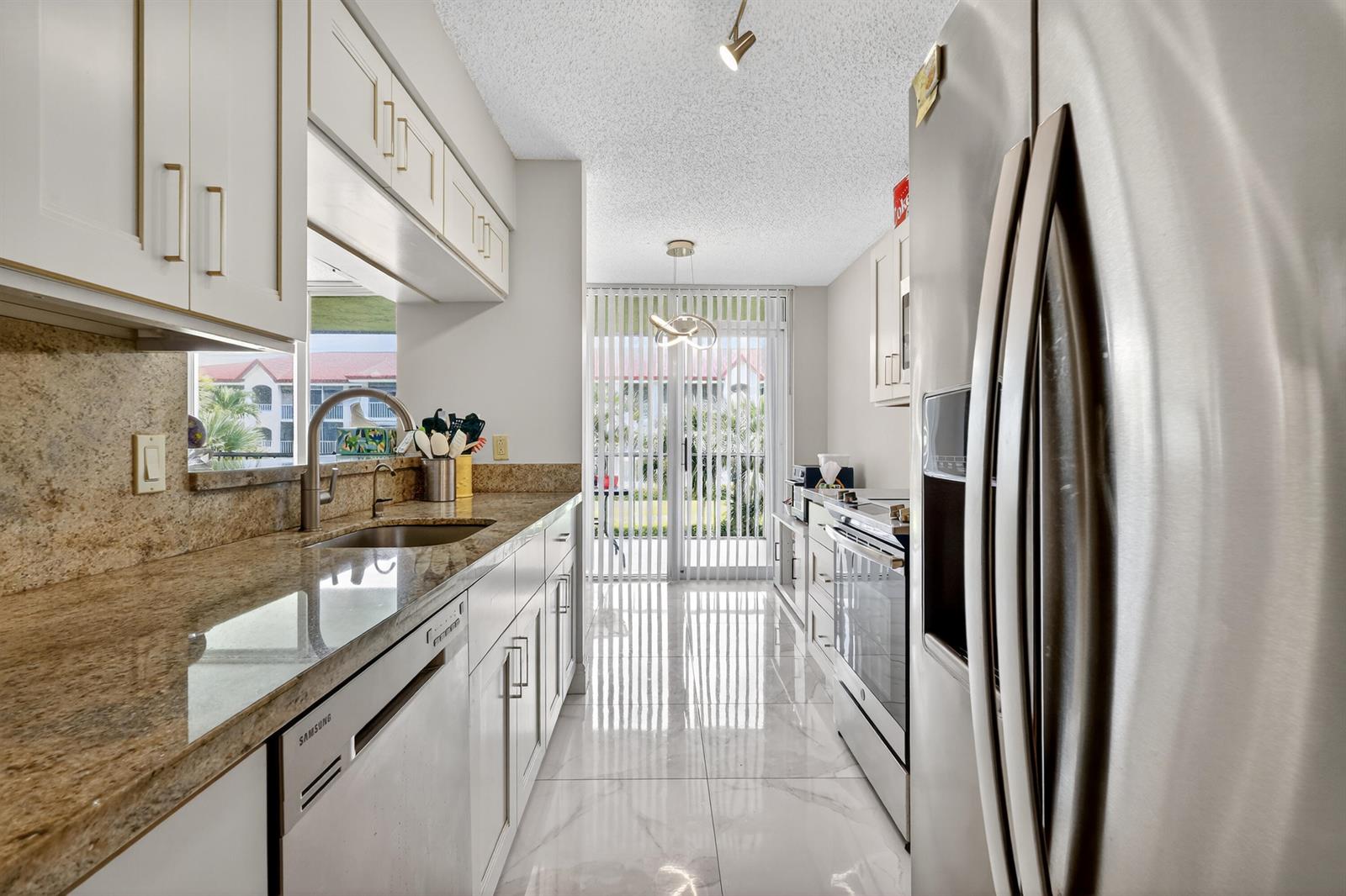A galley kitchen features white cabinets, granite countertops, stainless steel appliances, and tile flooring — 110 Half Moon Circle # D2, Hypoluxo FL 33462, HYPOLUXO, FL