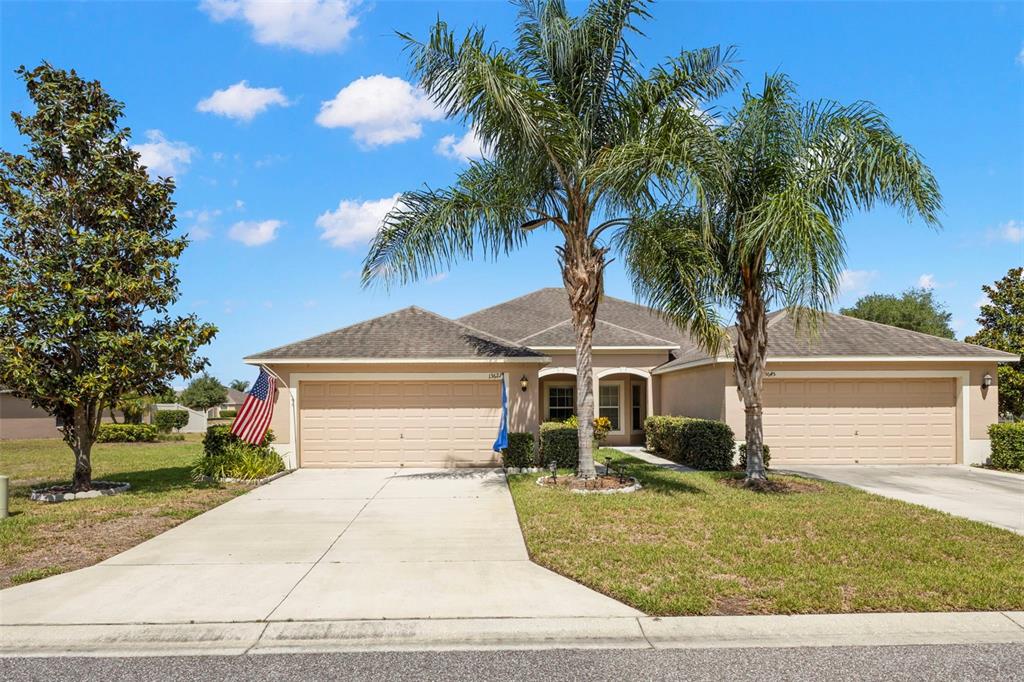A single-story house with two garage doors, palm trees, and an American flag — 13627 CREST LAKE DRIVE, HUDSON, FL