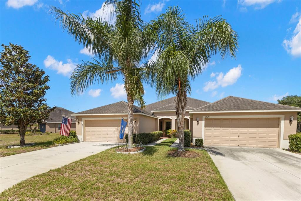 A single-story house with two garage doors, two palm trees, and a flag in front — 13627 CREST LAKE DRIVE, HUDSON, FL
