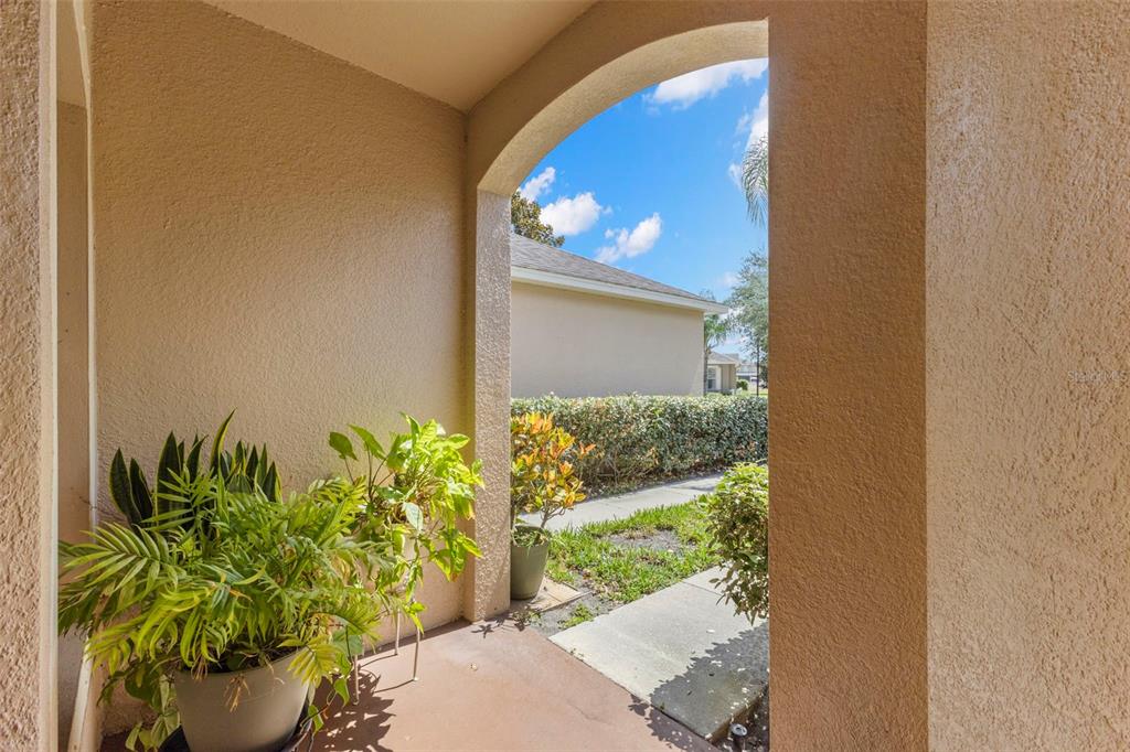 A covered entryway features a potted plant and an arched opening looking toward a sidewalk — 13627 CREST LAKE DRIVE, HUDSON, FL