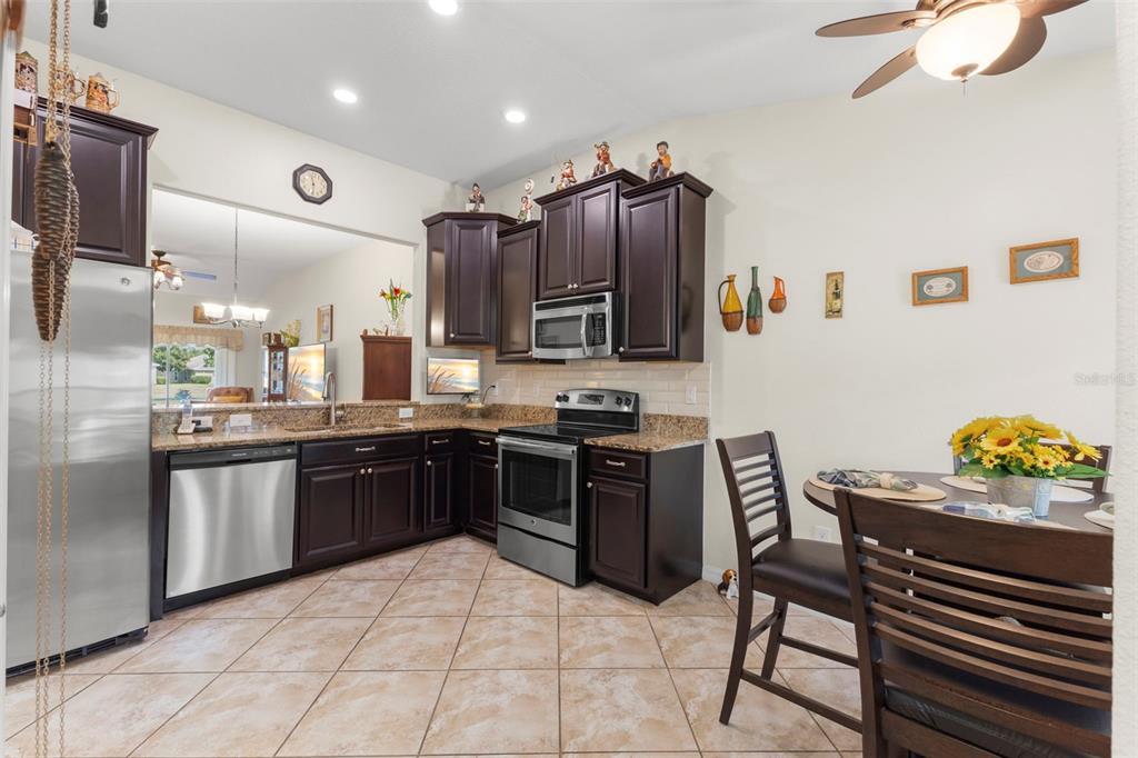 A kitchen features dark wood cabinets, stainless steel appliances, granite countertops, and tile flooring — 13627 CREST LAKE DRIVE, HUDSON, FL