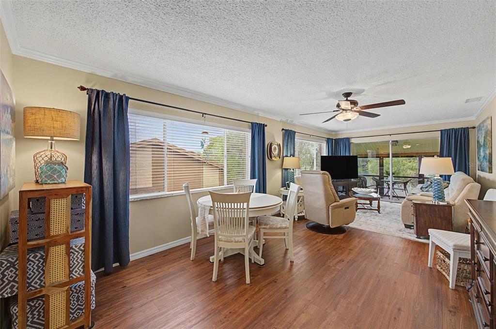 An open-concept living and dining area features wood-look flooring, a ceiling fan, and large windows — 4015 DAVIT DRIVE, NEW PORT RICHEY, FL