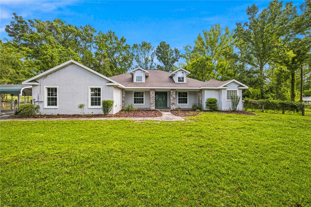 A single-story gray house with a stone-accented entrance and two dormer windows sits on grass — 5259 SE 38TH STREET, OCALA, FL